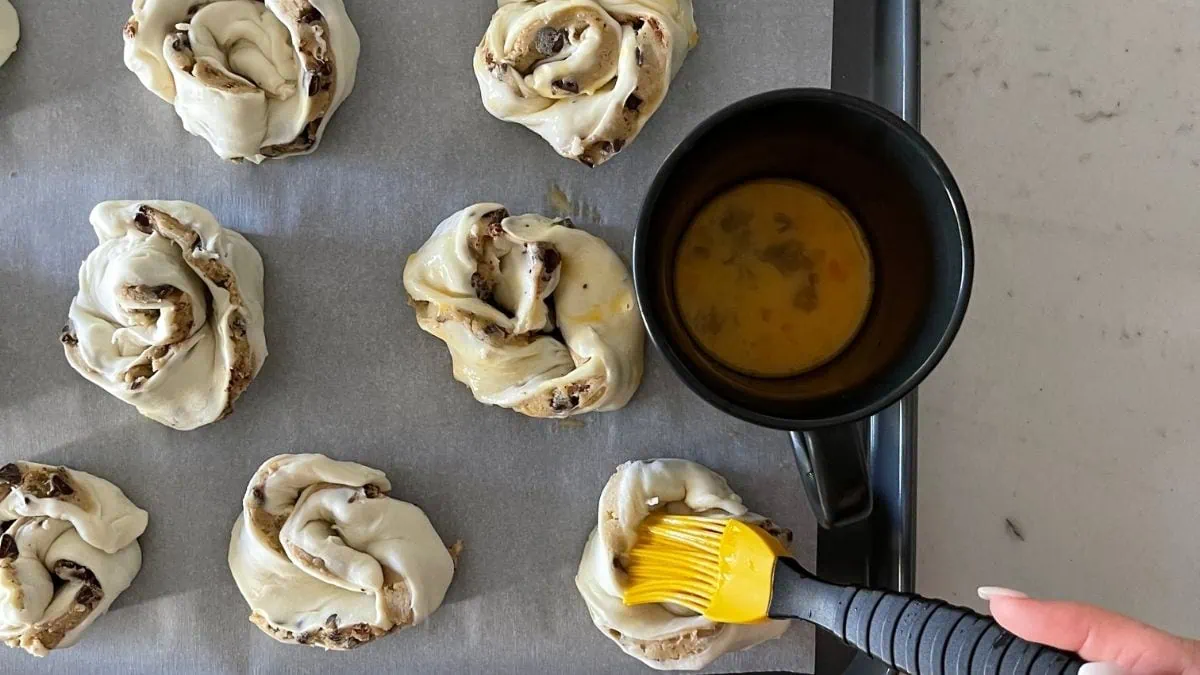 pastry rolls coated with egg wash. and a cup of egg wash with a pastry brush
